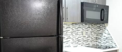 Una cocina con un refrigerador negro, un microondas y un protector contra salpicaduras de azulejos.