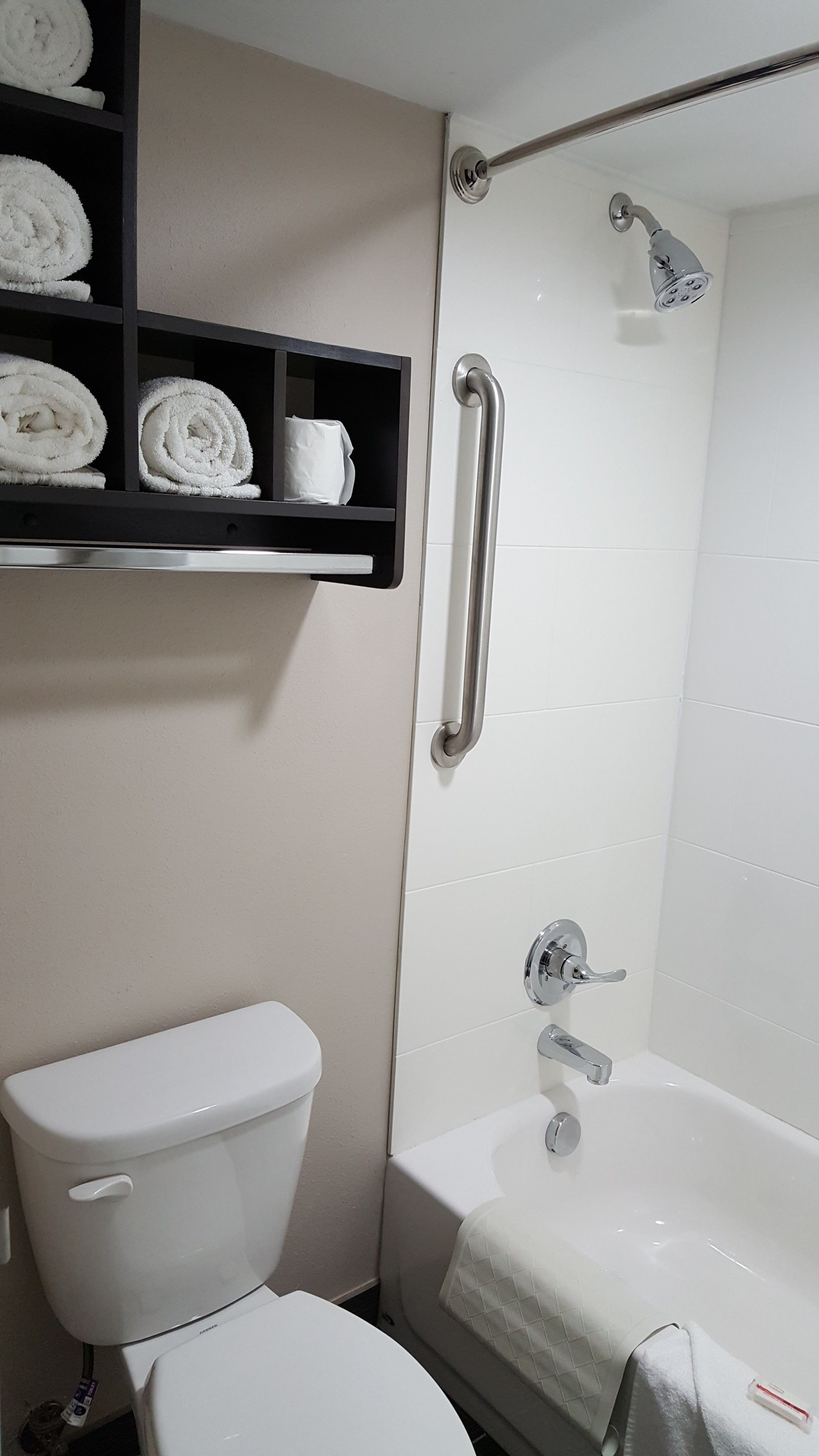 A bathroom with a toilet, a shower with a grab bar, and a shelf with towels.