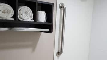 Une salle de bain équipée de toilettes, d’une douche avec une barre d’appui et d’une étagère avec des serviettes.