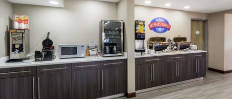 A breakfast area with a microwave, coffee maker, and a refrigerator. There is a sign that reads "Breakfast Corner".