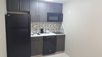 A compact kitchen with dark cabinetry, a built-in microwave, a coffee maker, and a dishwasher.