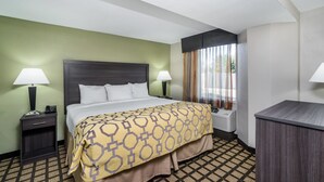 Quarto de hotel com cama, duas mesas de cabeceira com luminárias, escrivaninha e janela com cortinas.