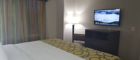 Habitación de hotel con una cama, un televisor de pantalla plana montado en la pared, una mesita de noche y una lámpara.