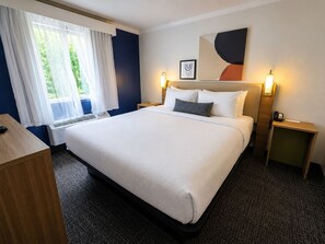 A hotel room with a large bed, bedside tables, a desk, and a window with curtains. - Spark by Hilton Lake George Outlets (Lake George)