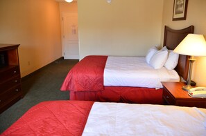 A hotel room with two beds, a wooden nightstand with a lamp, a telephone, and a wooden dresser. - Spark by Hilton Lake George Outlets (Lake George)