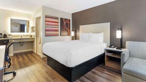 Ein Hotelzimmer mit einem großen Bett, einem Schreibtisch mit Stuhl, einem Nachttisch mit Lampe und einem durchgegangene Tür erkennbaren Badezimmer.