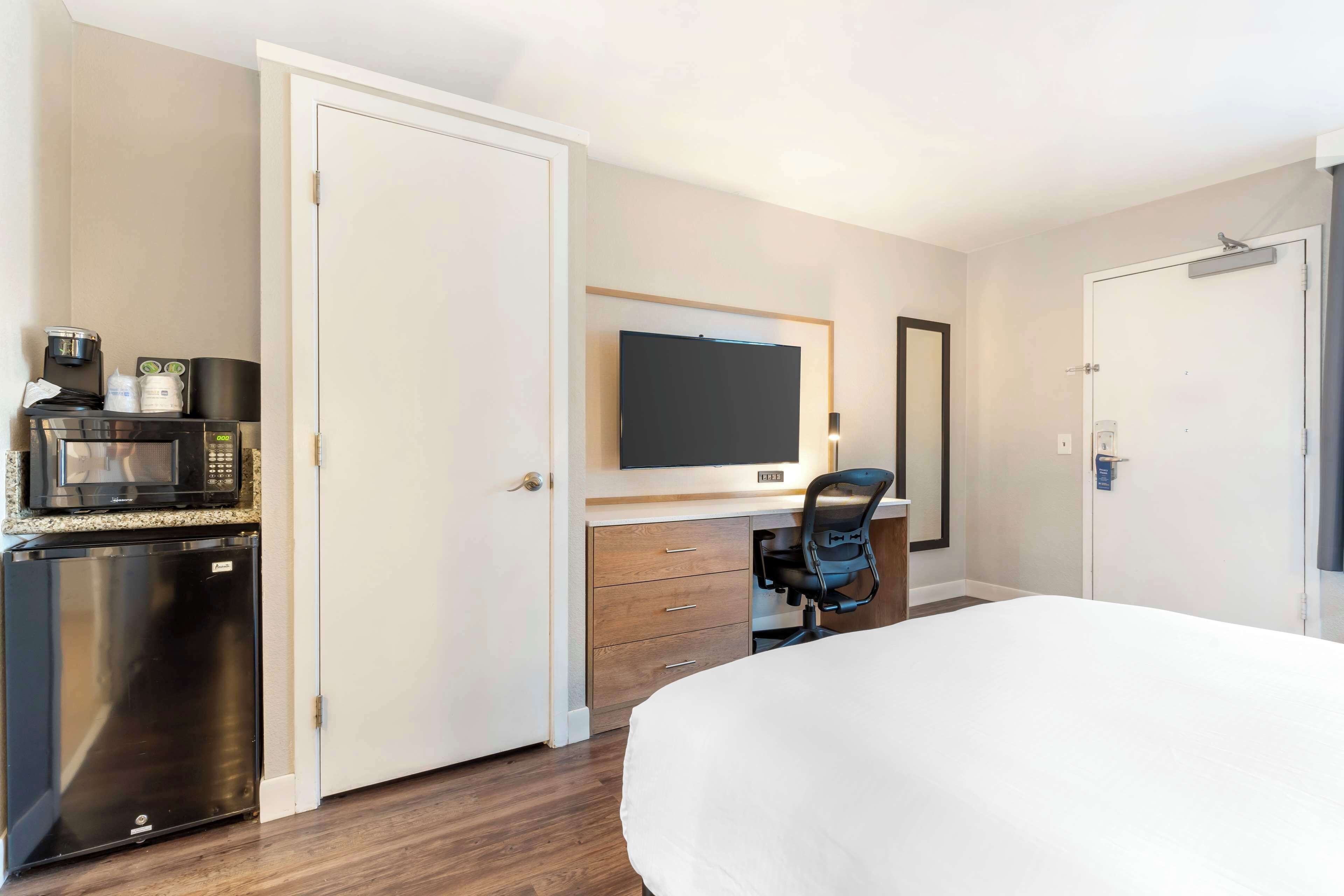 A hotel room with a bed, a desk with a computer, a microwave, and a refrigerator.
