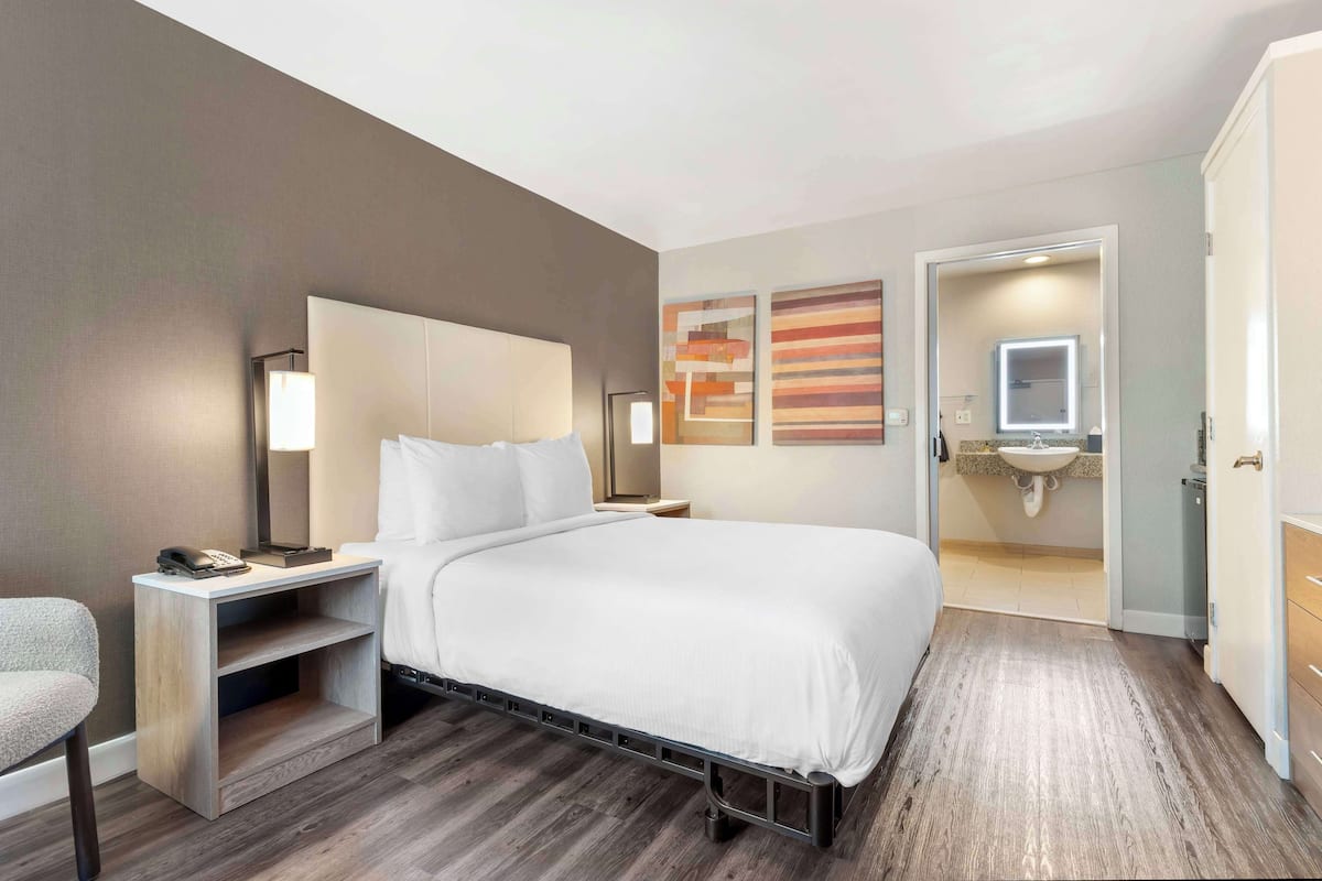 A hotel room with a bed, bedside tables, a chair, a desk, a lamp, a mirror, and artwork on the wall.
