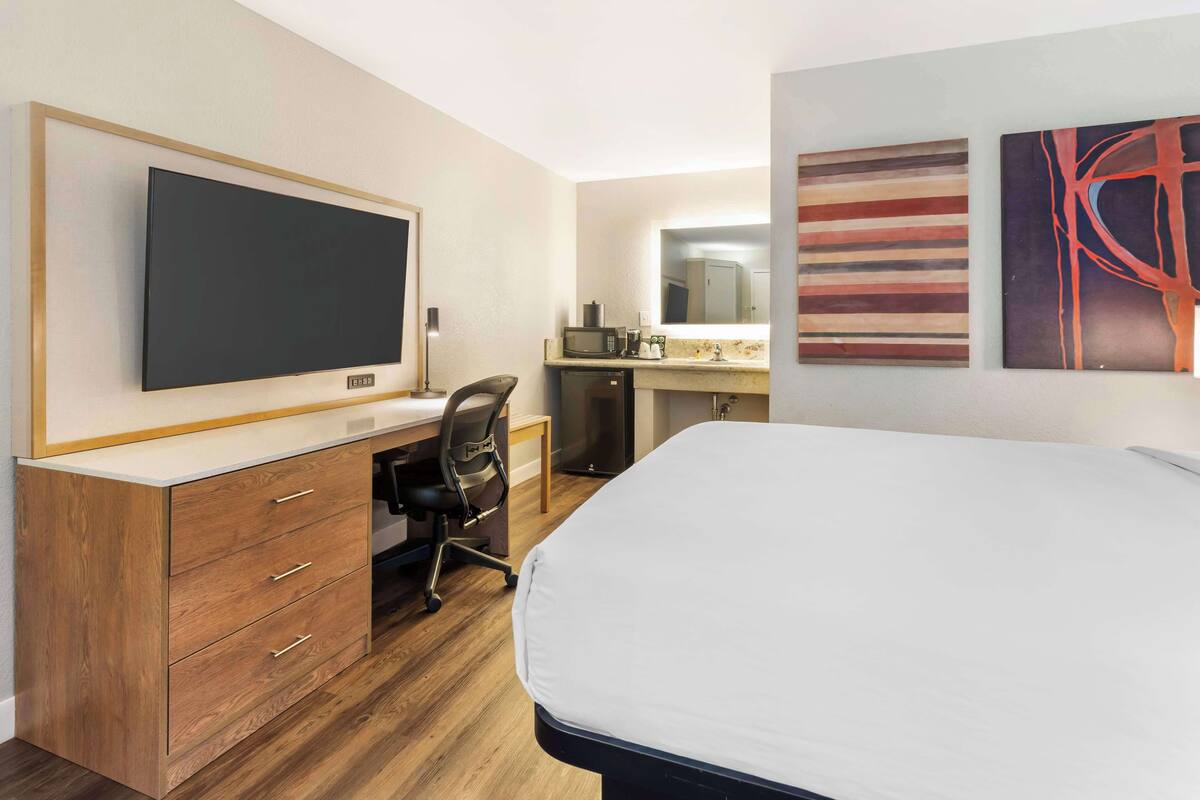 A hotel room with a bed, a desk with a chair, a flat-screen TV, a microwave, and a sink.