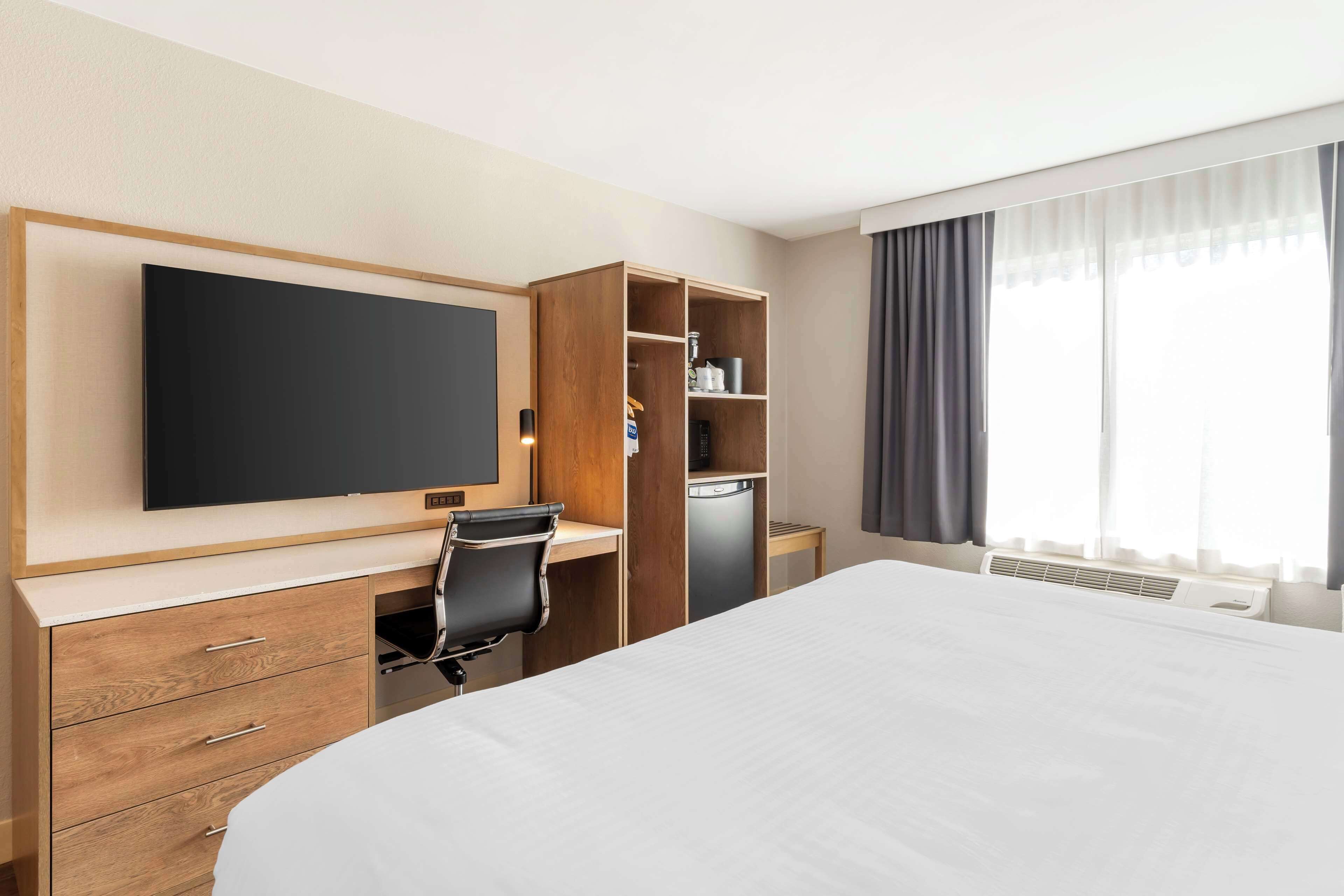 A hotel room with a bed, a desk with a chair, a television, a wardrobe, and a window with curtains.