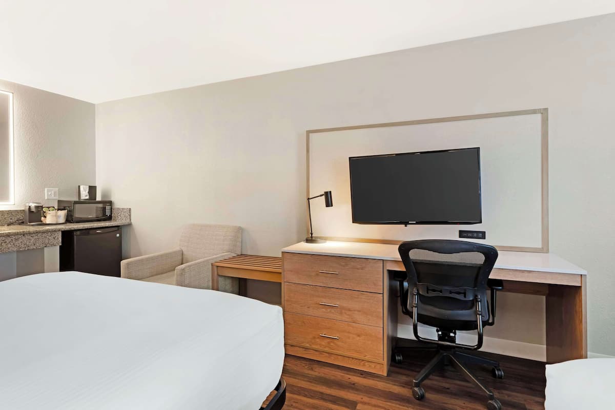 A hotel room with a bed, a desk with a computer, a chair, a TV, and a microwave.