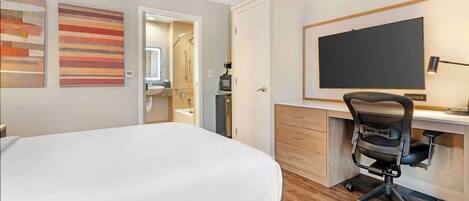 A hotel room with a bed, a desk with a computer, a TV, and artwork on the walls.