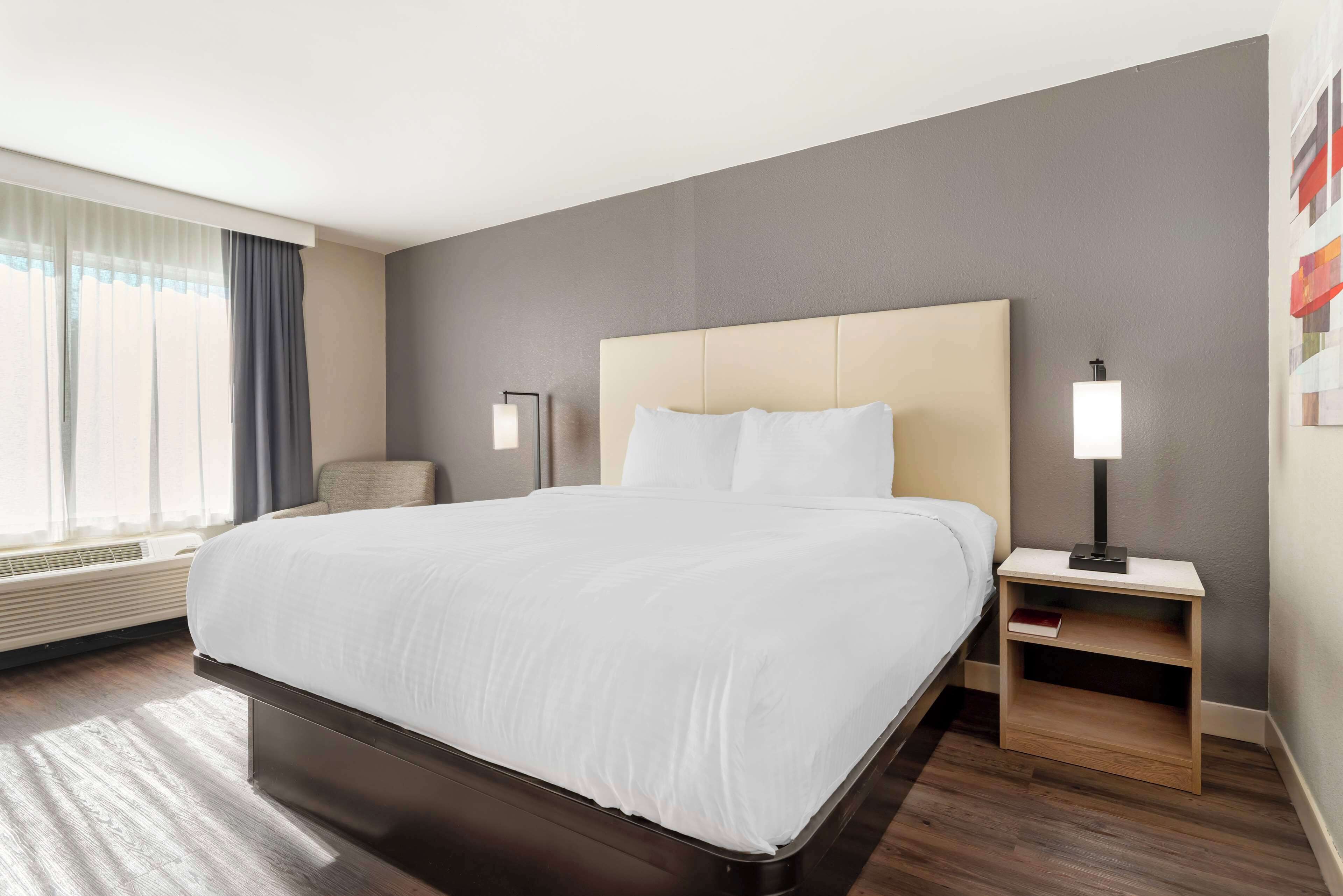 A hotel room with a large bed, bedside tables, a chair, and a window with curtains.