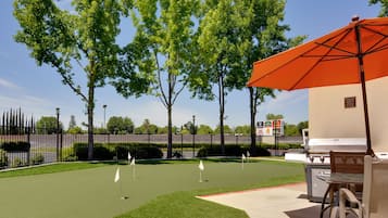 An outdoor patio with a grill, umbrella, and golf putting area.