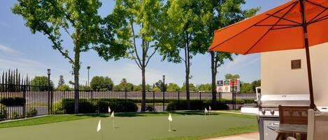An outdoor patio with a grill, umbrella, and golf putting area.