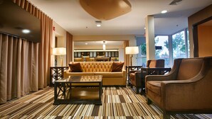 Eine Hotellobby mit Streifenmuster-Teppich, einer Couch, Sesseln, einem Couchtisch und einem Essbereich im Hintergrund.