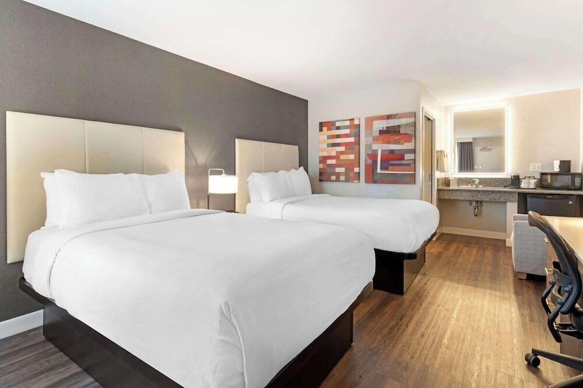 Habitación de hotel con dos camas, un escritorio, una silla, un microondas y un espejo de baño.