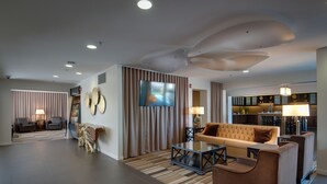 Eine moderne Hotelhalle mit einer Sitzecke, einem Fernseher und einer Küche im Hintergrund.