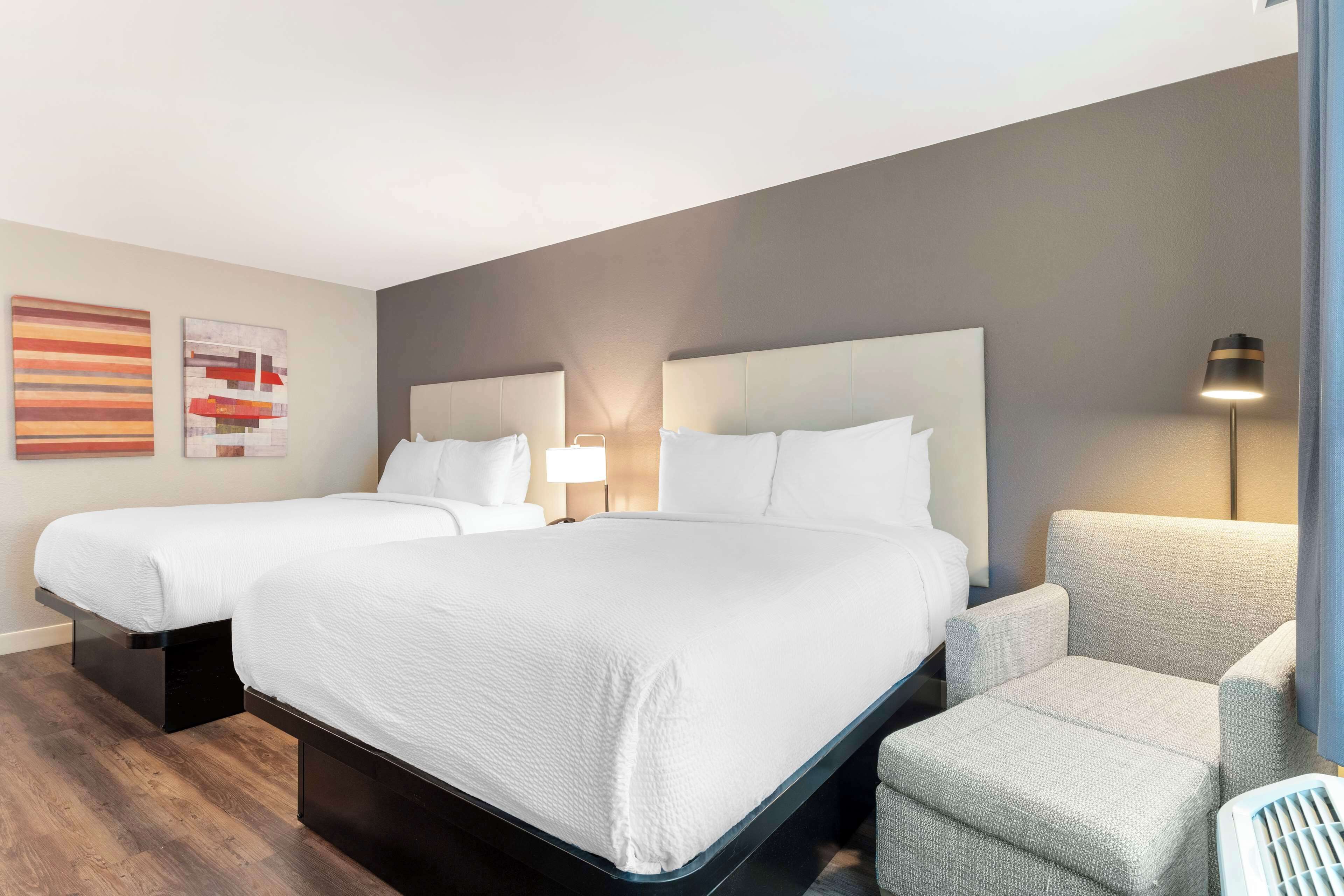 Una habitación de hotel con dos camas, una silla y una obra de arte en la pared.