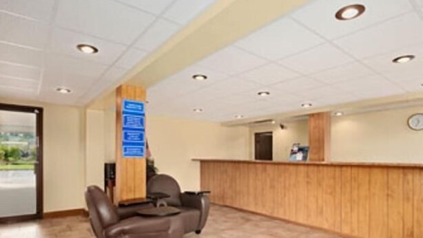 A reception area with a wooden reception desk, a seating area with two chairs, and a tiled floor. - Hilltop Inn (Pittsburgh)