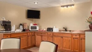 A kitchen with wooden cabinets, a microwave, a coffee maker, and a television mounted on the wall. - Hilltop Inn (Pittsburgh)