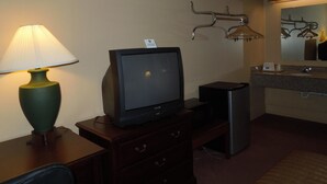 A hotel room with a television on a wooden stand, a lamp, a mirror above the sink, and a coat rack with hangers. - Hilltop Inn (Pittsburgh)
