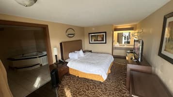 Une chambre d’hôtel avec un lit, un bureau, un miroir et une salle de bain visible à travers une porte ouverte.