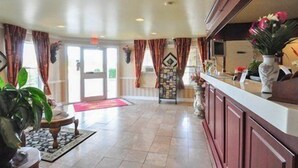 A spacious hotel lobby with a reception desk, a large window with curtains, and a tiled floor.