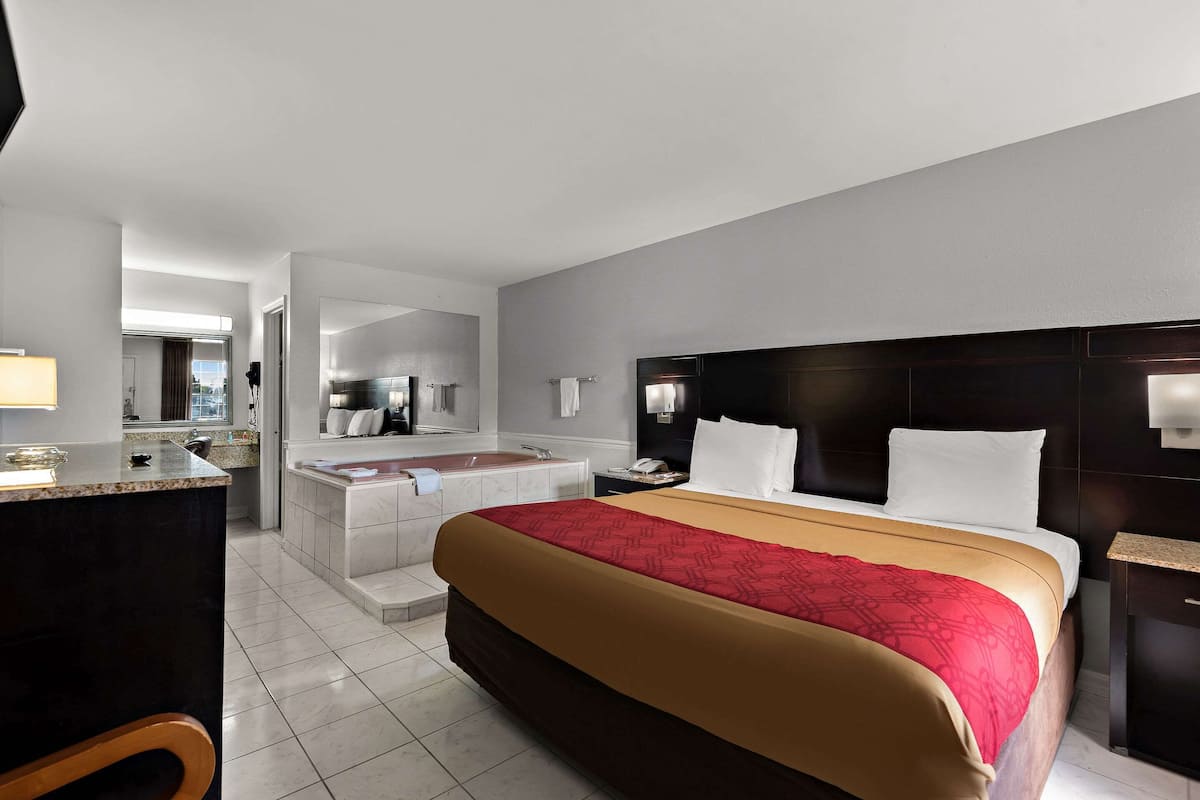 A hotel room with a large bed, a separate bathroom with a bathtub, a desk, and a chair.