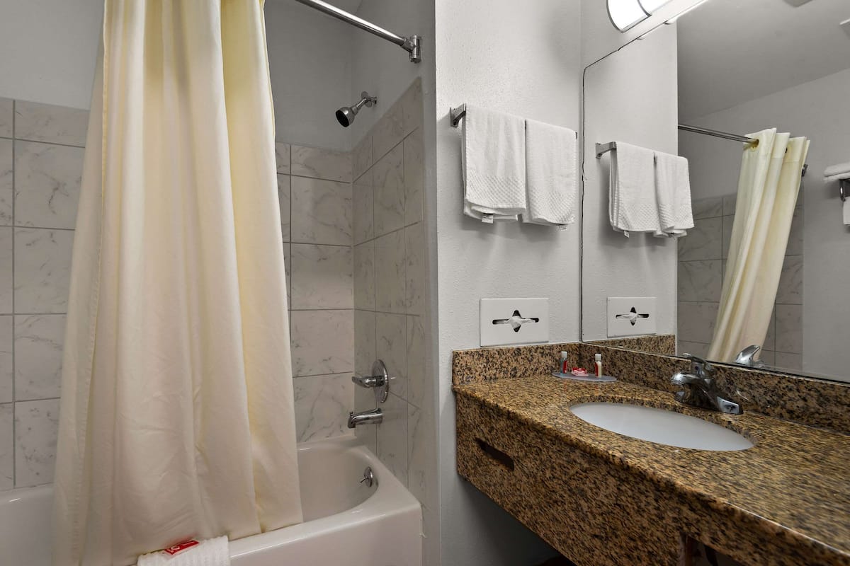 A bathroom with a bathtub, a sink with a granite countertop, and a mirror with two towels hanging on the wall.