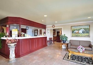 A reception area with a wooden counter, a sofa, a coffee table, and a painting on the wall. - Econo Lodge Princess Anne (Princess Anne)