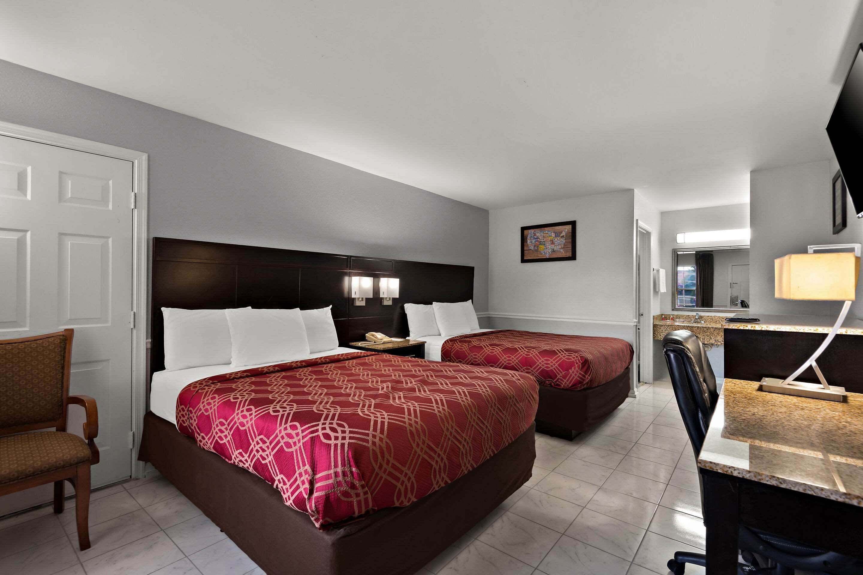 Habitación de hotel con dos camas, un escritorio, una silla, televisión y baño visible a través de una puerta abierta.