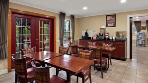 A dining area with a wooden table and chairs, a kitchen area with a refrigerator and coffee maker, and a view through the glass doors.