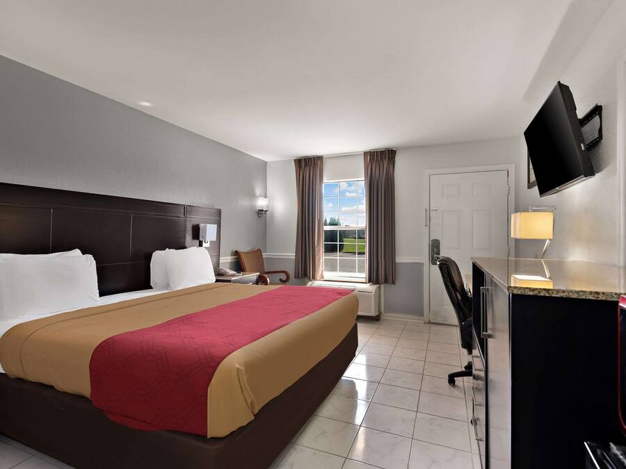 Habitación de hotel con una cama grande, un escritorio con silla, un televisor montado en la pared y una ventana con cortinas.