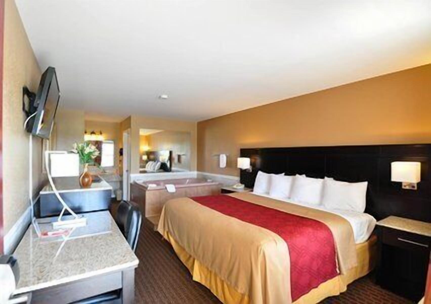 A hotel room with a bed, a desk, a chair, a TV, and a bathroom visible in the background.