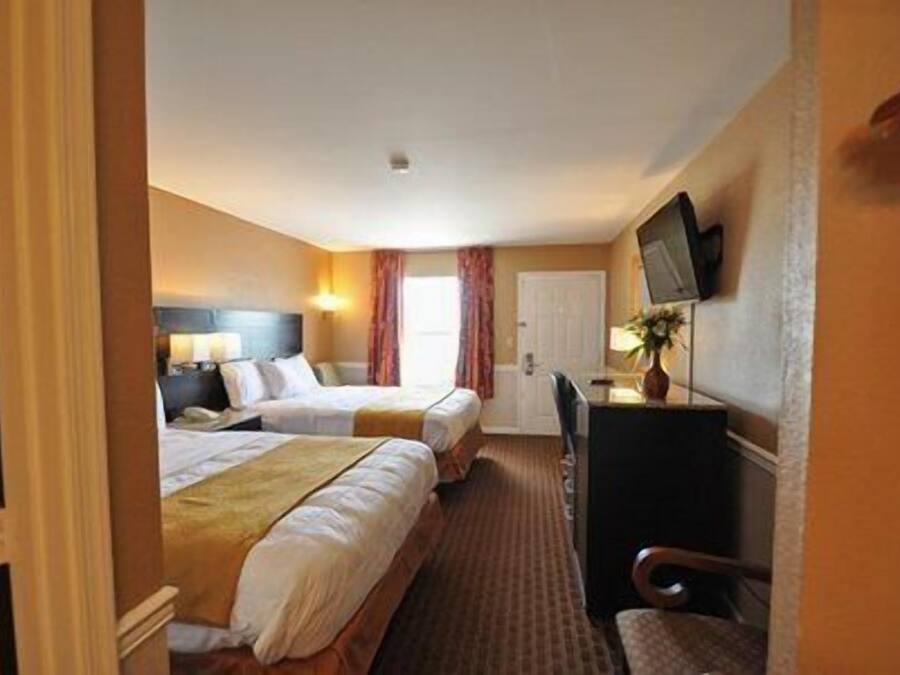A hotel room with two beds, a desk, a chair, a television, and a window with curtains.