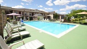 A swimming pool with lounge chairs and umbrellas, surrounded by a building with multiple balconies.