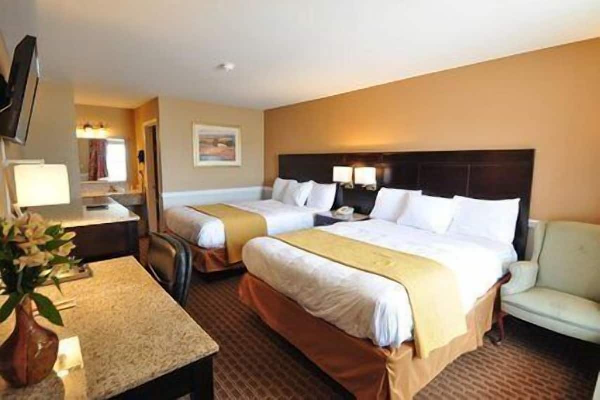 A hotel room with two beds, a desk, a chair, and a television.