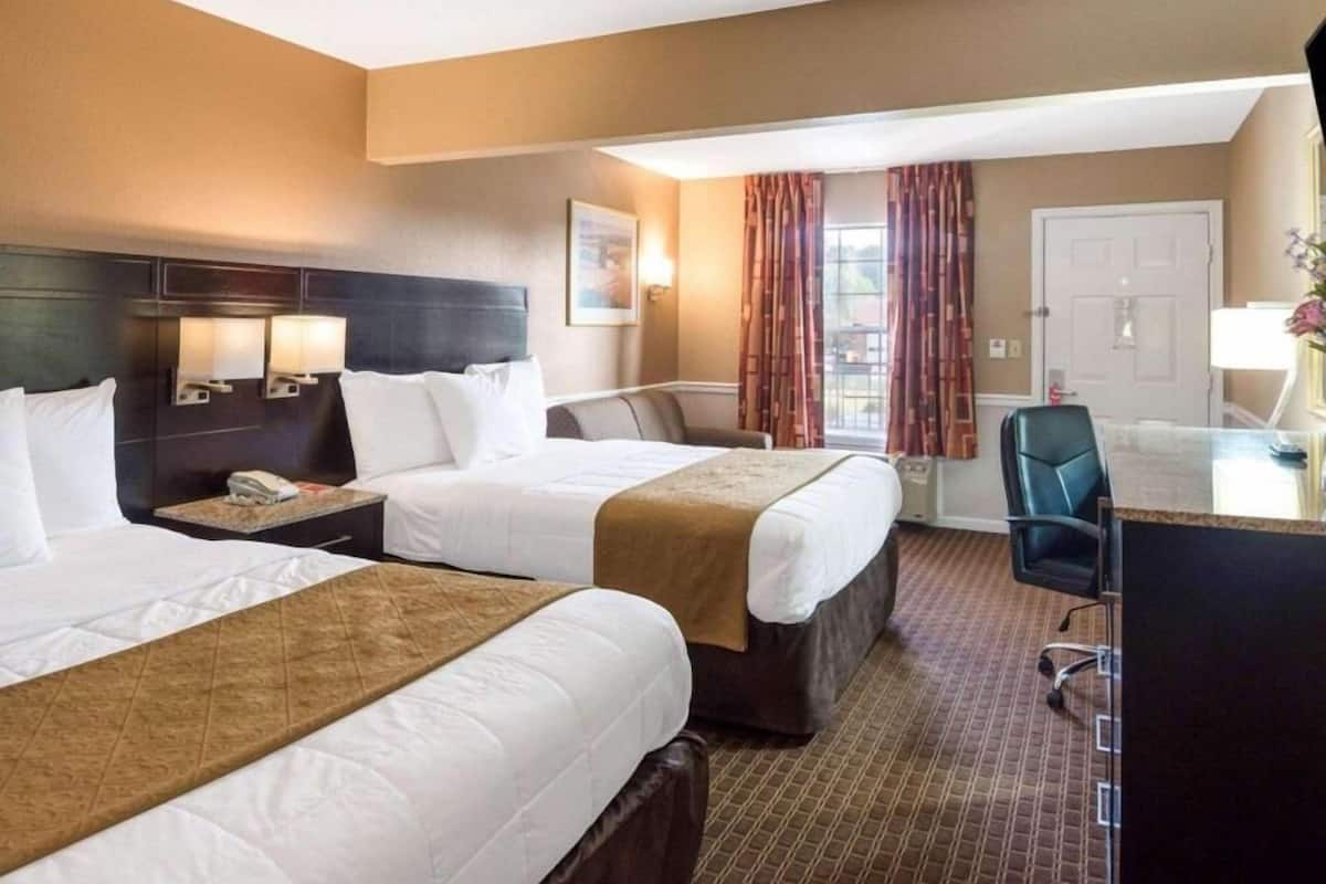 A hotel room with two beds, a desk, a chair, and a view of the outdoors.