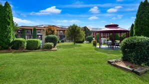 A well-maintained lawn with a gazebo, neatly trimmed hedges, and a building with a modern design in the background.