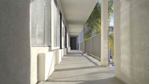 A corridor with a concrete floor and white walls, featuring large windows and a metal railing on one side. - Motel 6 Inglewood, CA (Inglewood)