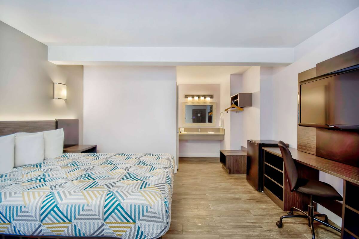 A hotel room with a bed, a desk, a chair, a TV, and a mirror.