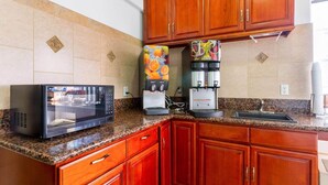 A kitchen with wooden cabinets, a microwave, a coffee machine, and a juice dispenser. - Motel 6 Inglewood, CA (Inglewood)