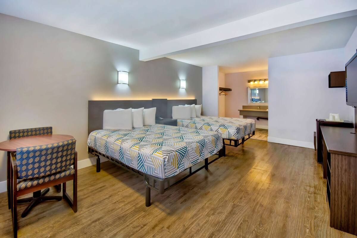A hotel room with two beds, a desk, and a chair.