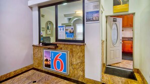A hotel reception area with a reception desk, a sign for room number 6, and a coffee sign. - Motel 6 Inglewood, CA (Inglewood)