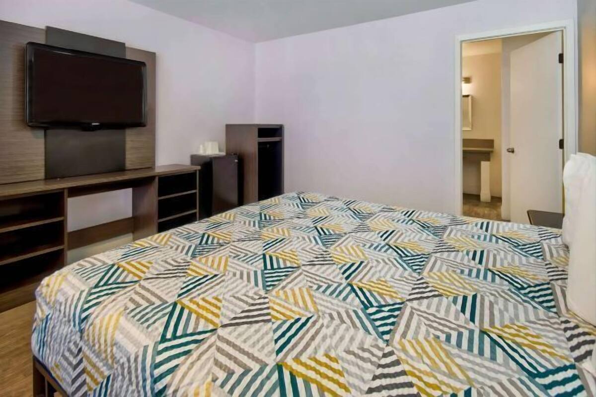 A hotel room with a bed, a TV mounted on the wall, a wardrobe, and a door leading to a bathroom.