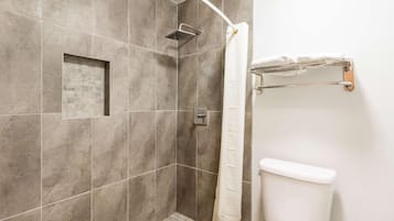 Un espace douche doté d’une cabine de douche en verre, de toilettes blanches et d’un porte-serviettes.