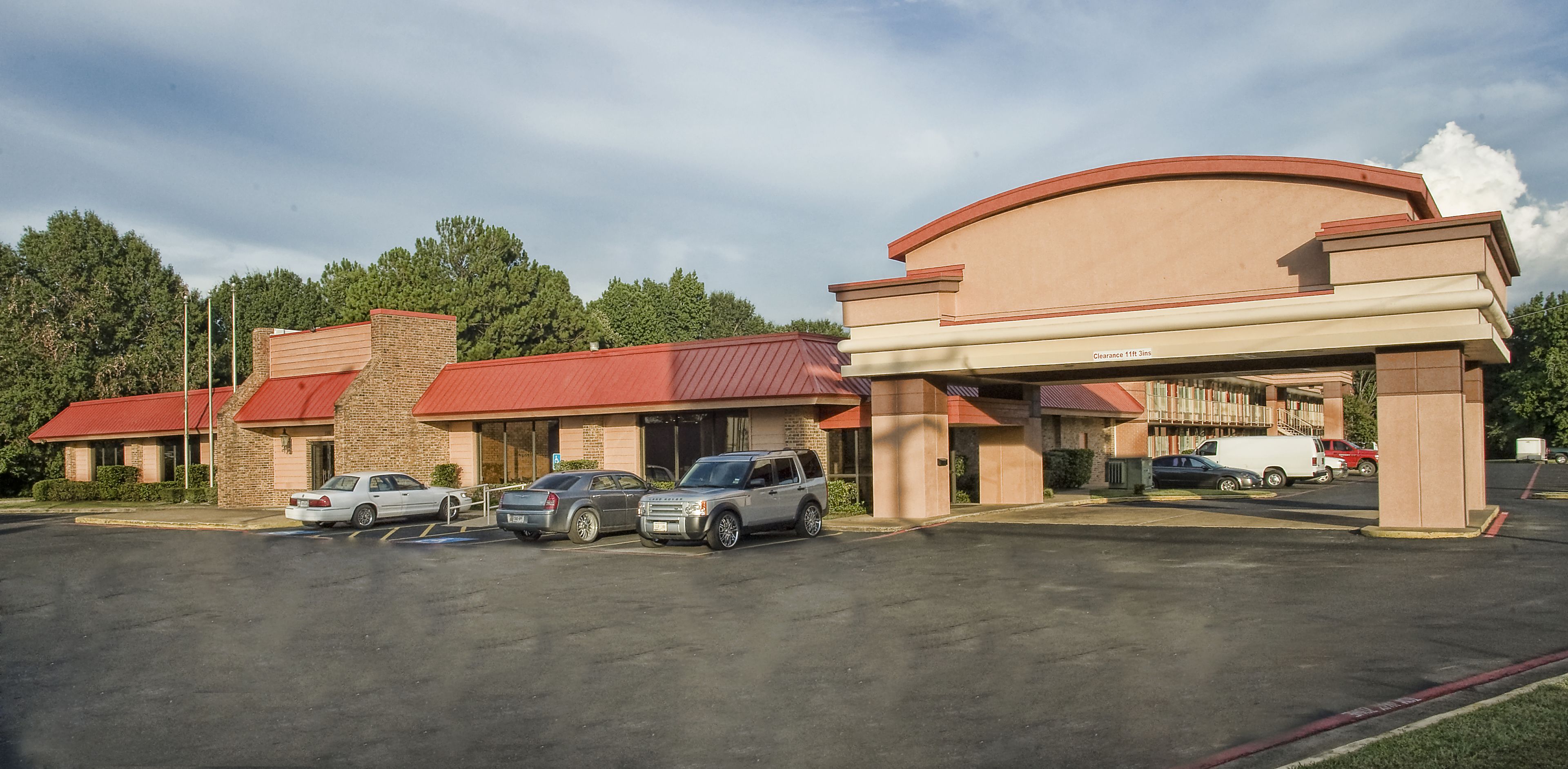 A hotel with a parking lot, multiple cars parked, and a large building with a curved roof.