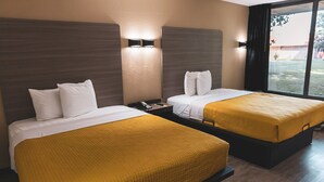 Une chambre d’hôtel avec deux lits, chacun recouvert d’une couvre-lit blanche et jaune, une table de chevet avec un téléphone et un luminaire fixé au mur.