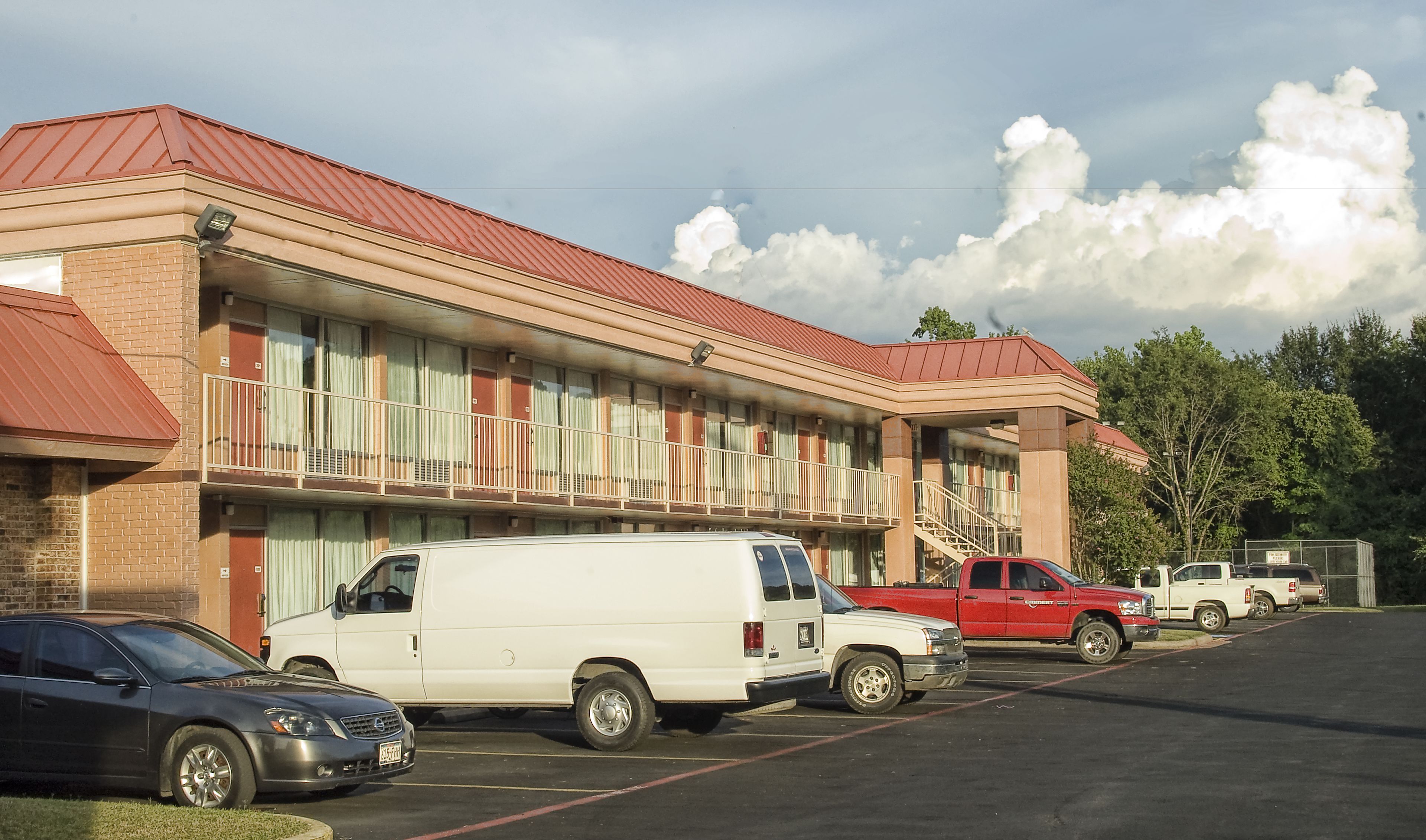 A motel with a red roof, multiple balconies, and a parking lot with several vehicles.